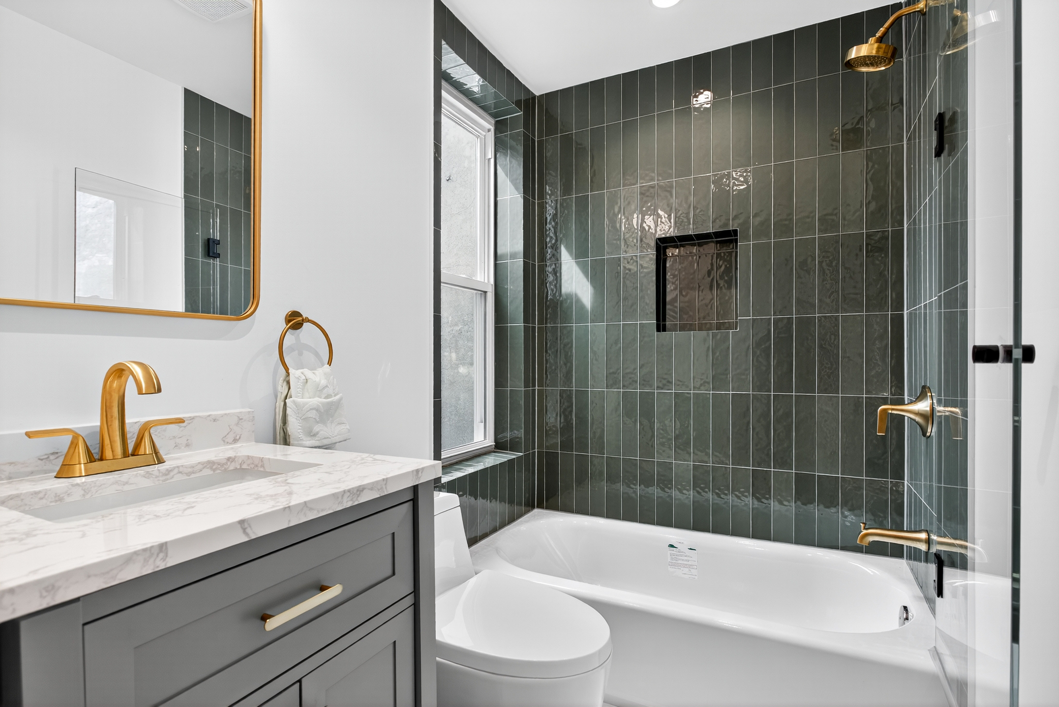 Bathroom details up close — stacked vertical tile, brass fixtures, custom vanity with quartz top