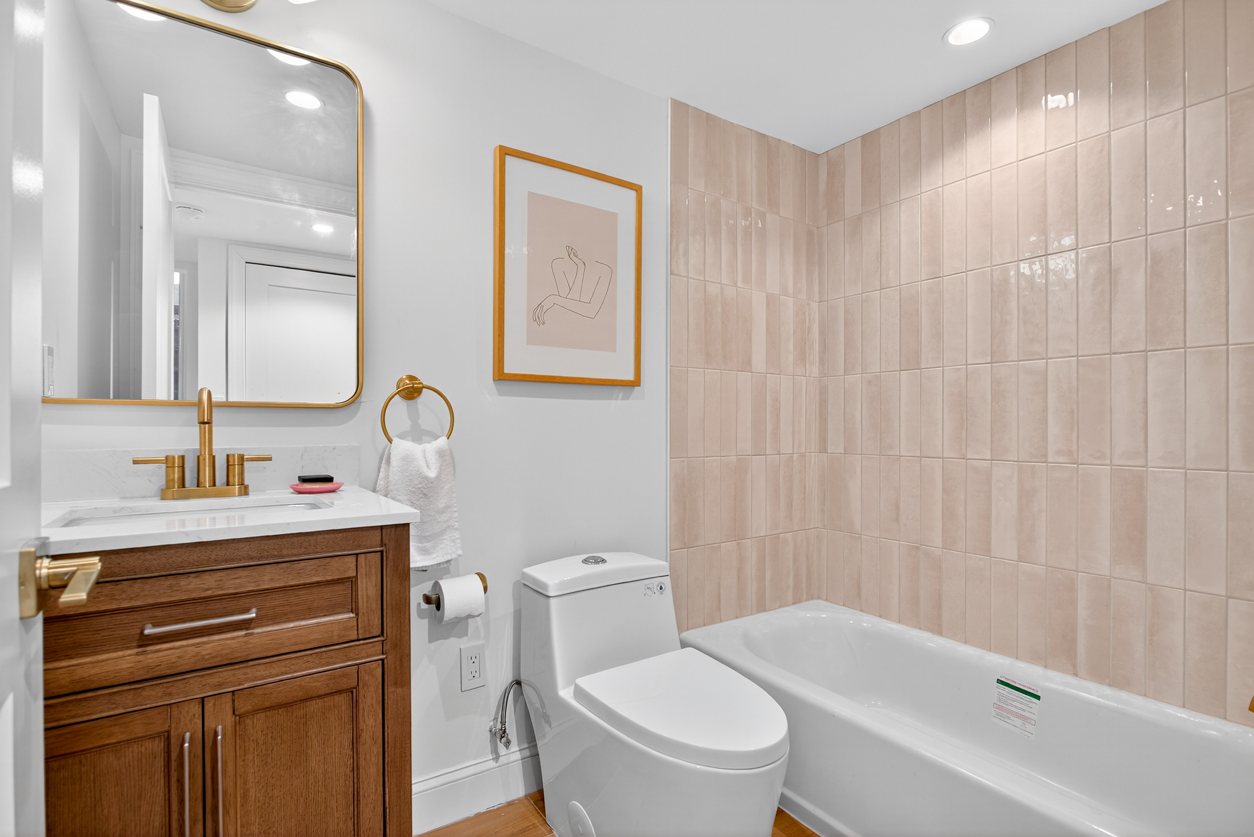 Basement bathroom with cream tile, warm wood vanity, and brass fixtures