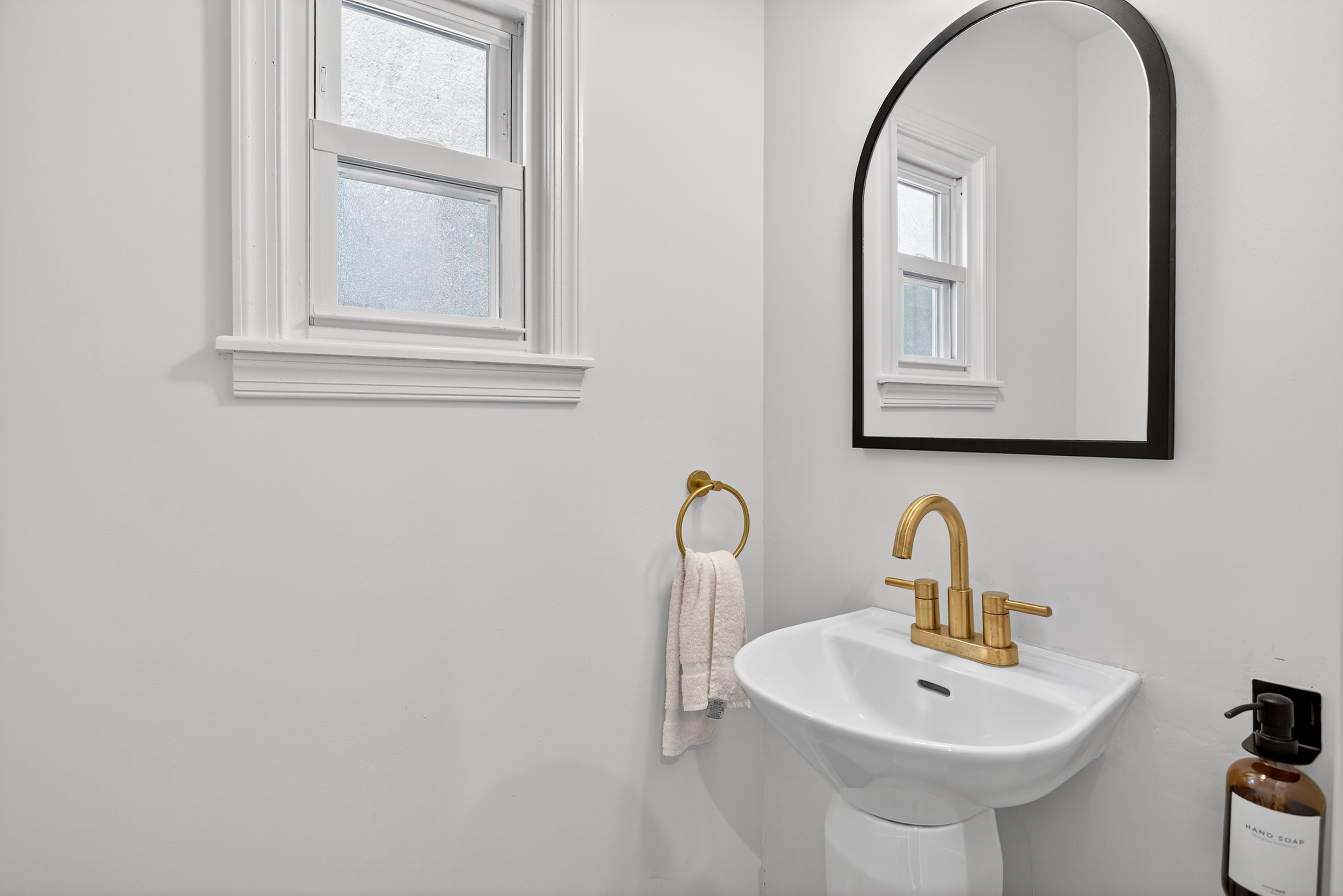 First-floor powder room with wall-mount sink, arched mirror, and brass faucet