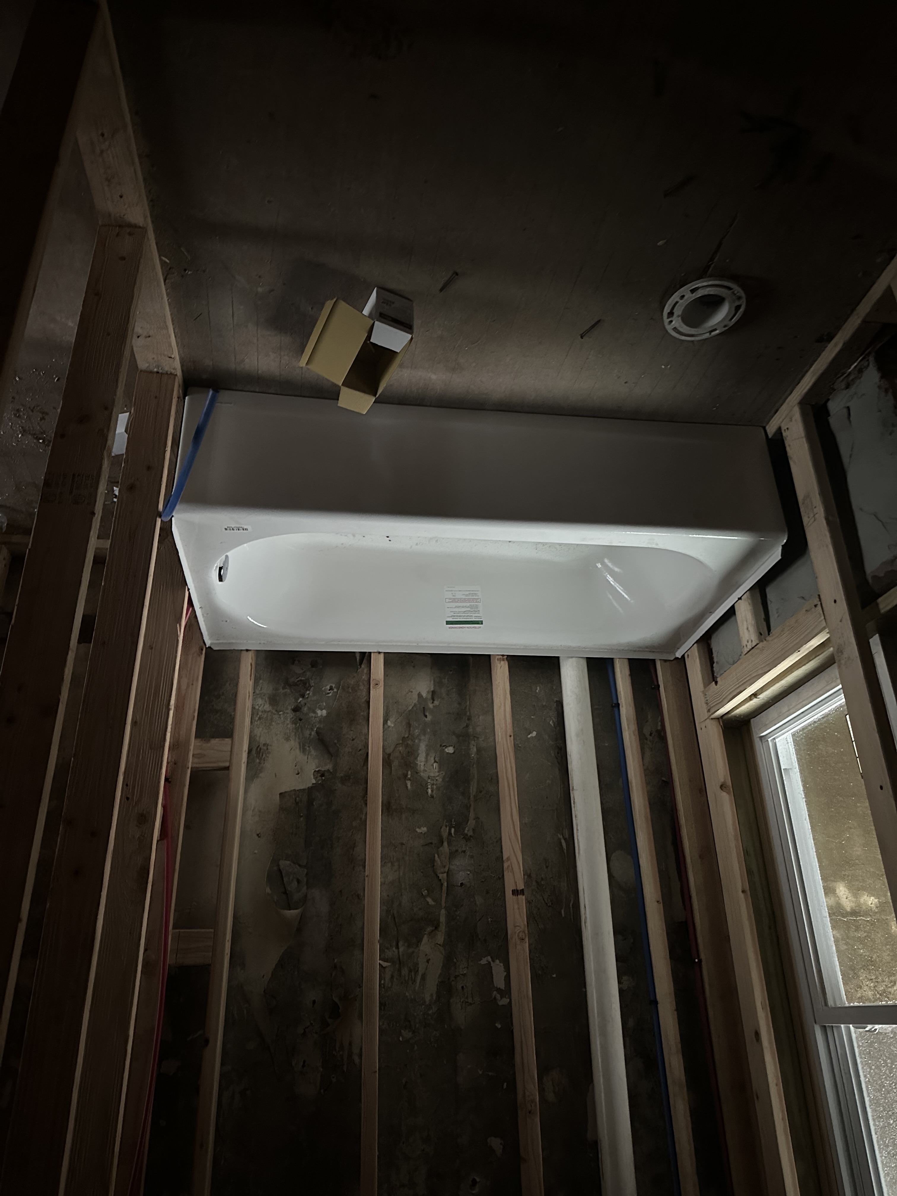E. Columbia Ave bathroom mid-build — walls opened to framing, tub installed, plumbing rough-in visible